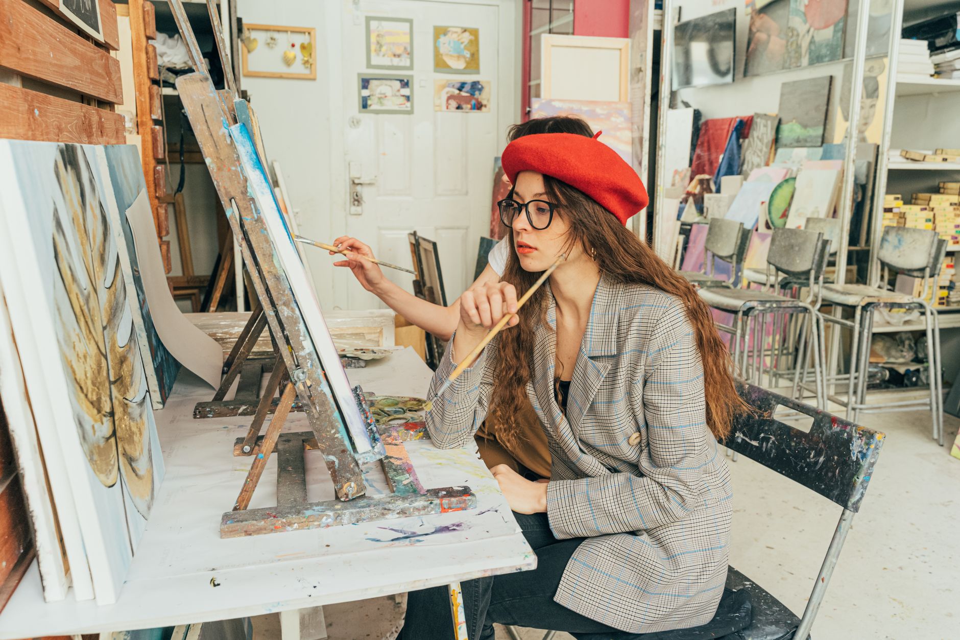 A young artist in a red beret paints attentively in an art studio full of canvases and supplies in Long Beach, CA